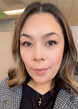 Woman with medium length wavy brown hair wearing a black and white jacket over black shirt
