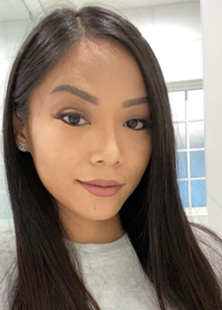 Woman with long, straight, dark hair wearing a light gray shirt silver earrings